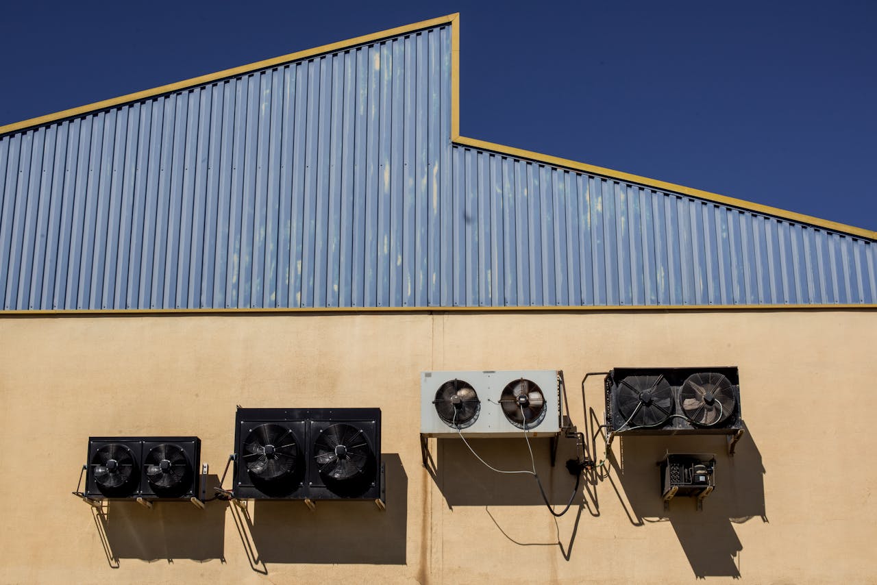 Exterior view of industrial air conditioning units mounted on a warehouse wall under clear blue sky.